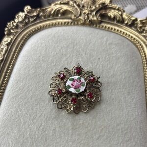 gold-tone filigree brooch with red rhinestones and a central guilloché enamel